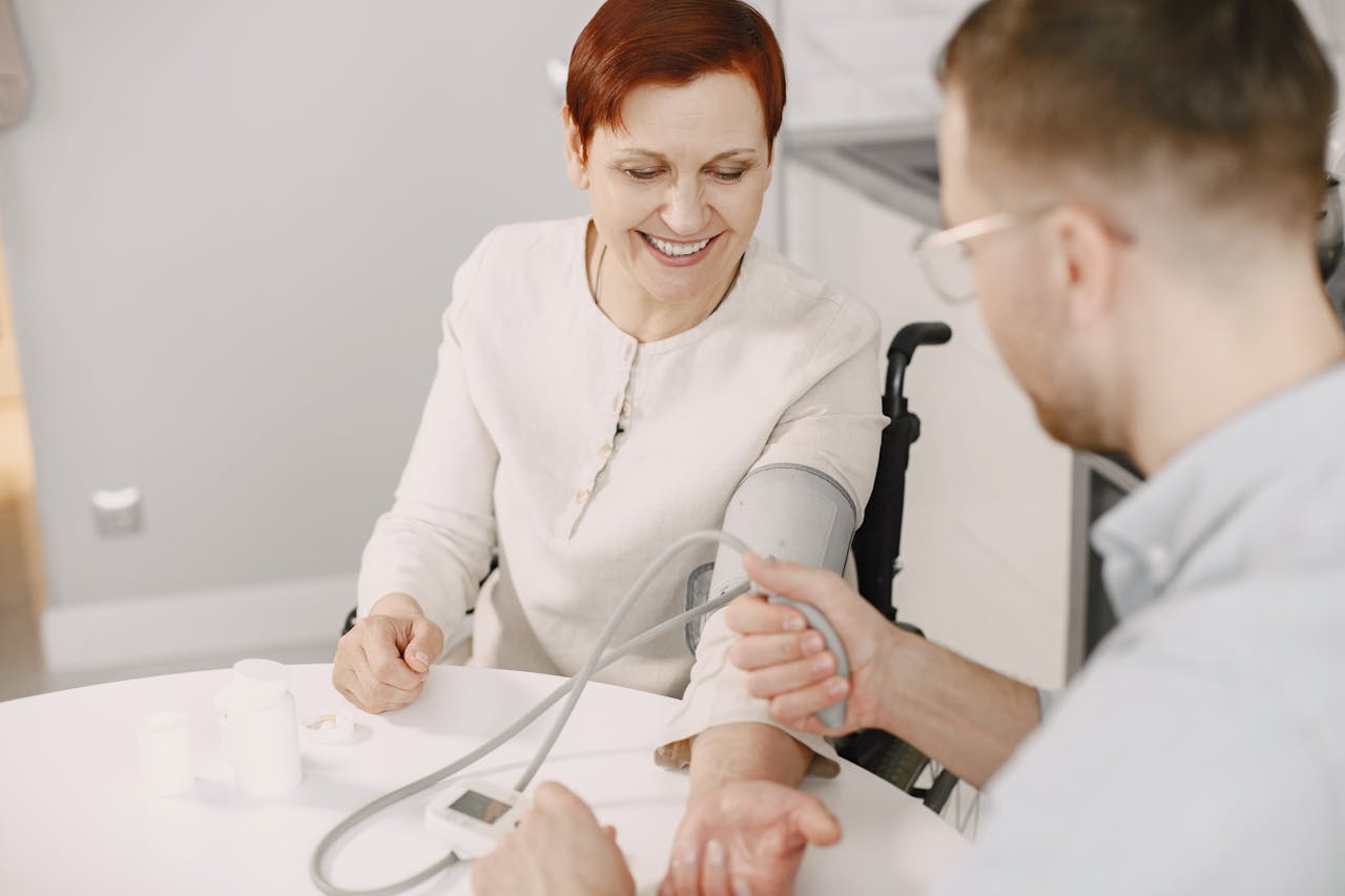 Man assisting elderly woman with blood pressure check at home in a friendly atmosphere.